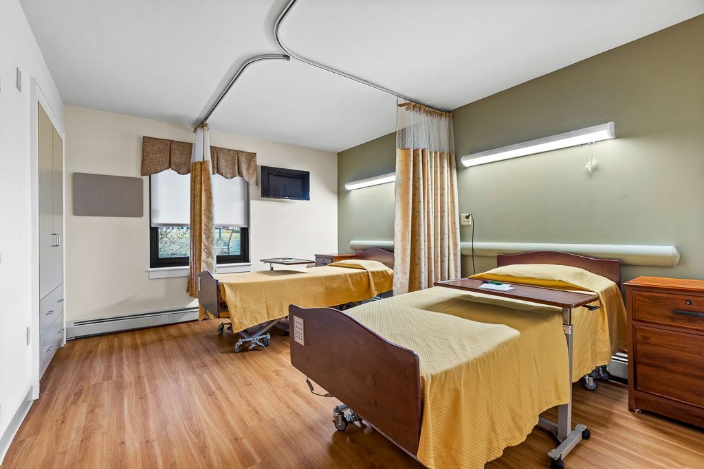 Hospital room with two beds, wood floors, curtains, and a television.