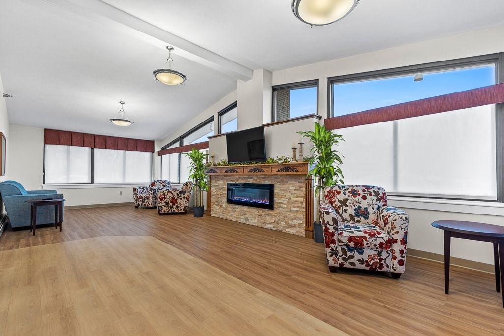 Lounge area with light wooden floor, fireplace, armchairs, large windows, and three hanging lights.