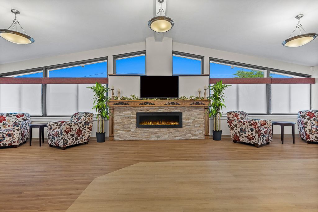 Spacious room with fireplace, armchairs, and large windows with blue sky visible.