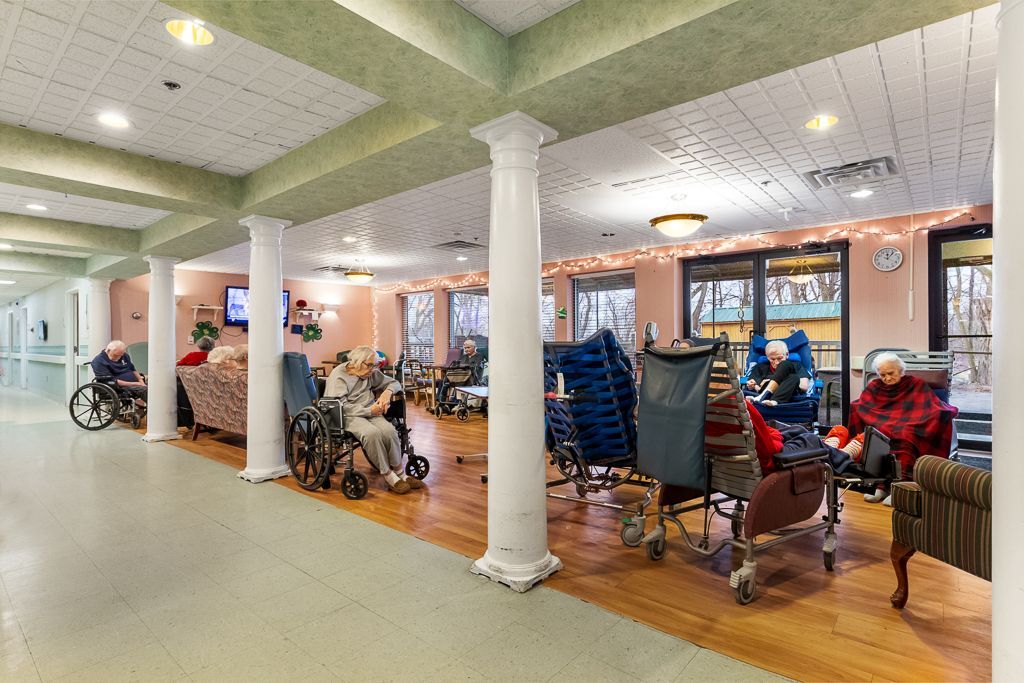 Long hallway with elderly people in wheelchairs and chairs; interior of a nursing home.