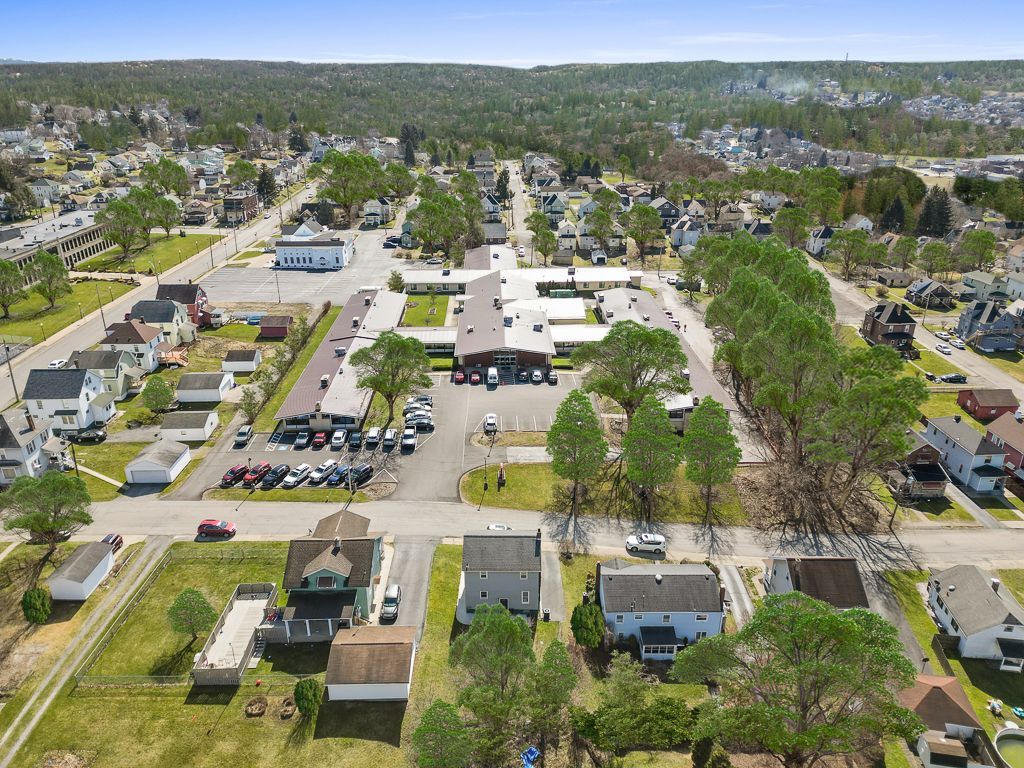 Aerial view of a town with houses, businesses, and a large building in the center, surrounded by trees and a clear sky.