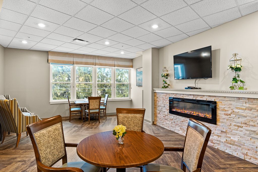 Cozy lounge area with fireplace, TV, round table, and chairs near windows.