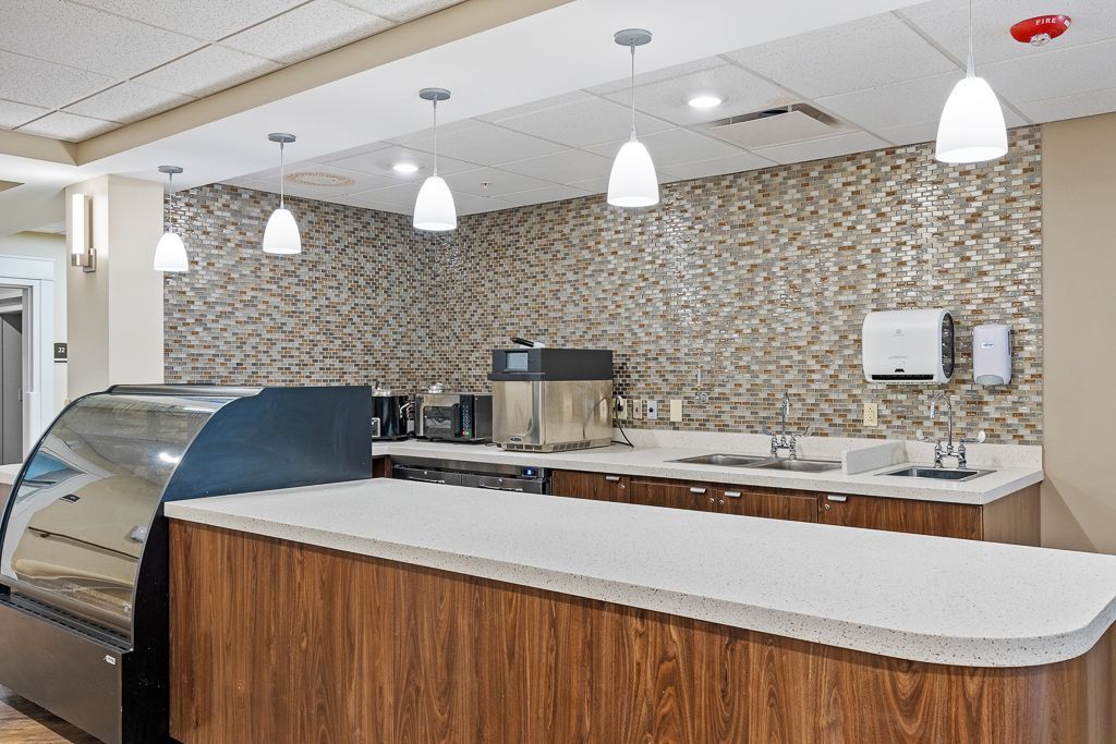 Cafeteria counter with wood cabinets, white countertop, stone backsplash, and hanging lights.