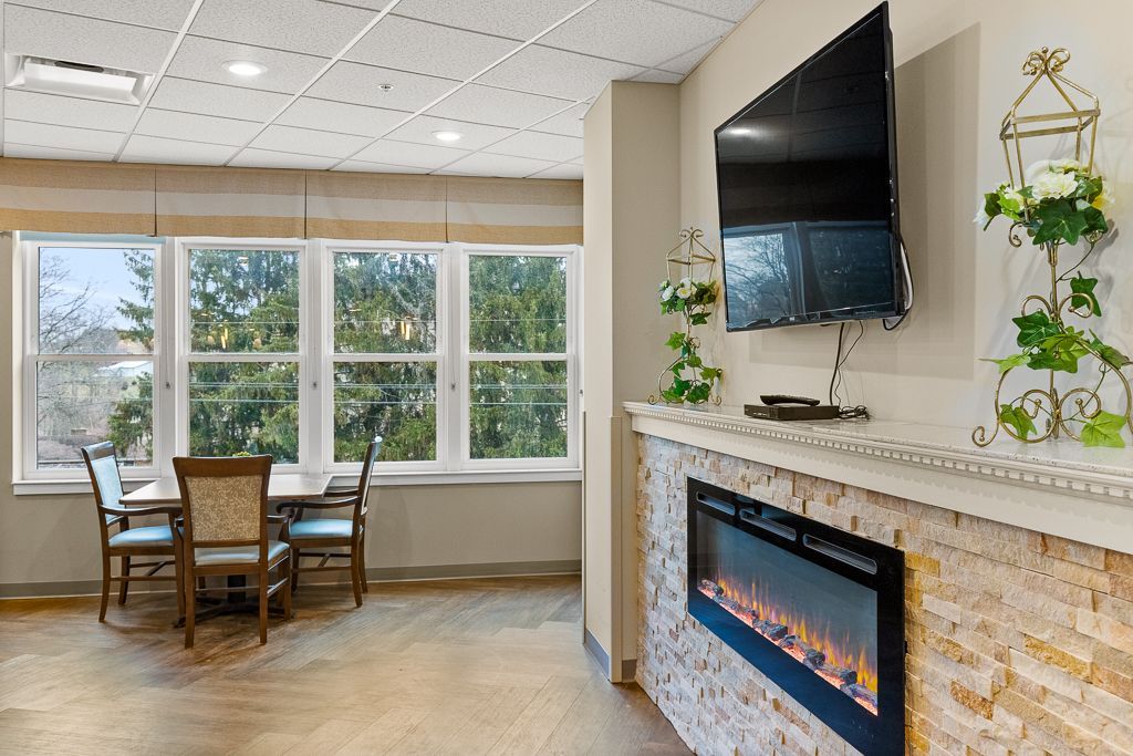 Interior shot of a room with a dining table by a window, a fireplace, and a mounted TV.