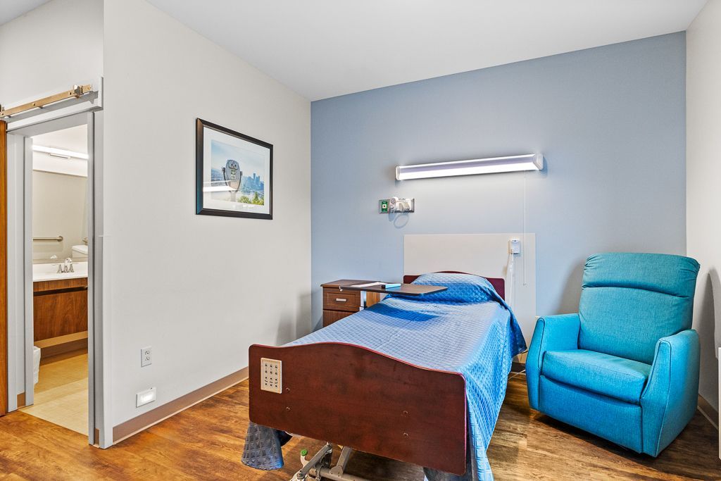 Hospital room with bed, recliner, and bathroom visible. Walls are blue and white.