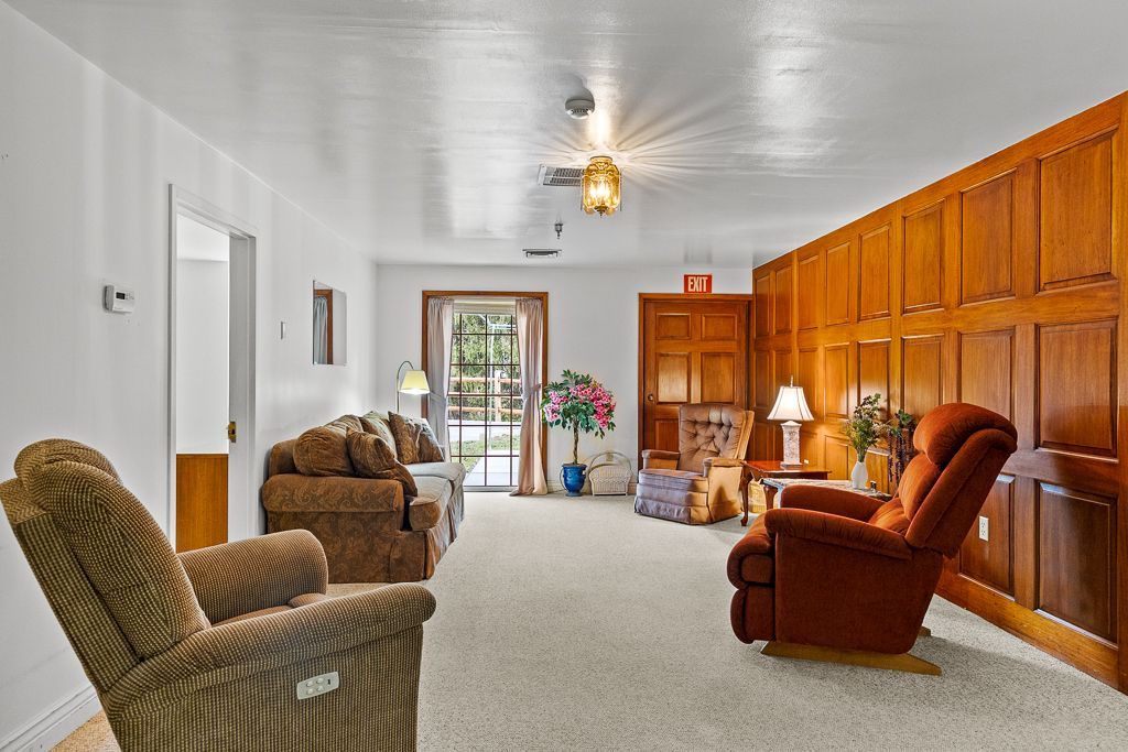 Cozy living room with wood paneling, recliner, couch, and sliding door to outdoor view. Beige carpet and ceiling.