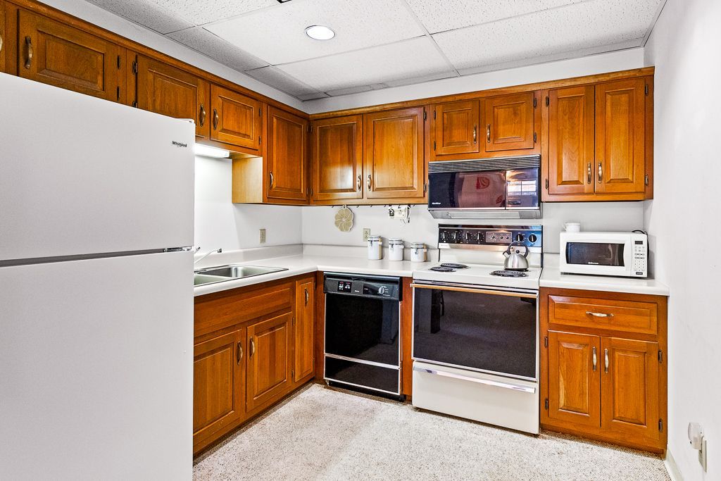 Kitchen with wooden cabinets, white appliances, and speckled floor.