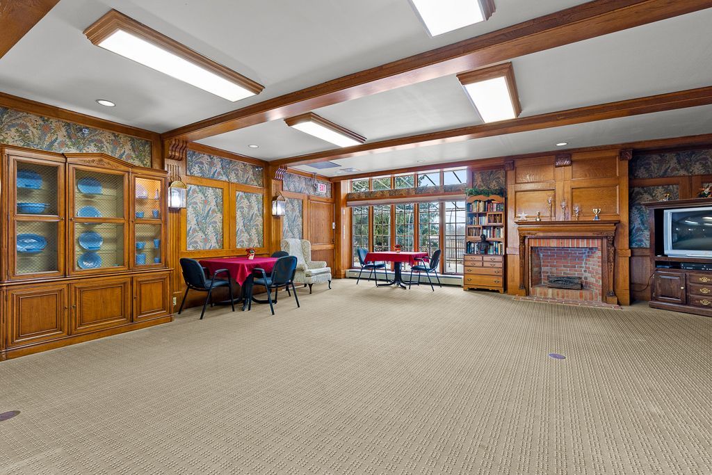 Spacious room with wood paneling, carpet, tables, and fireplace; glass cabinets on the left.
