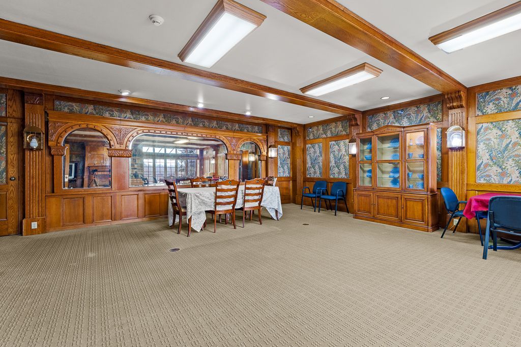A wood-paneled dining room with tables, chairs, cabinets, and a patterned carpet.