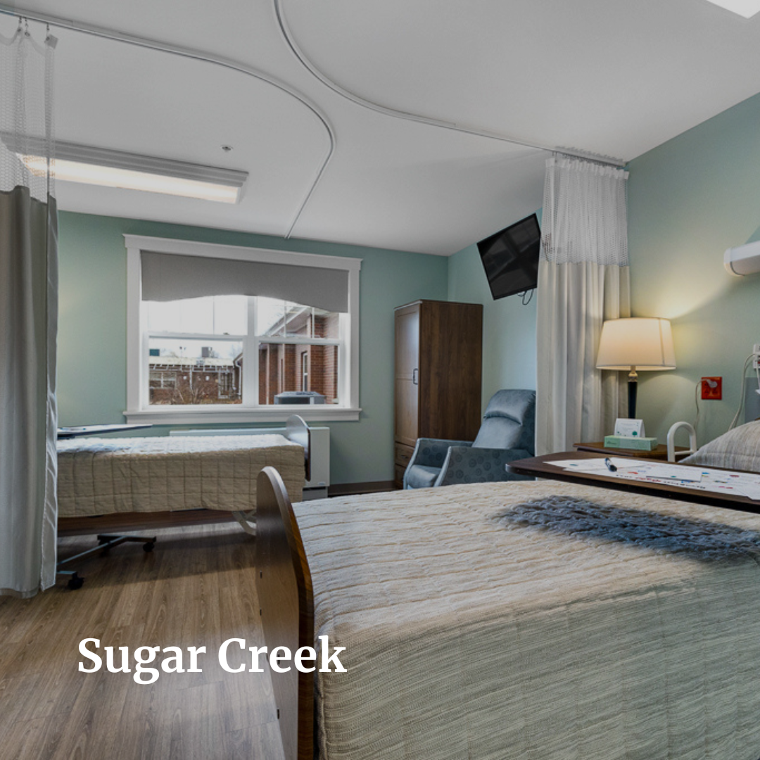 Hospital room with two beds, window, television, and furniture.