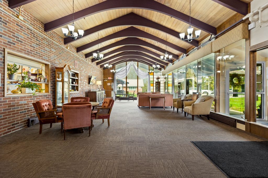 Spacious lobby with exposed beams, brick wall, seating areas, and large windows looking out onto greenery.