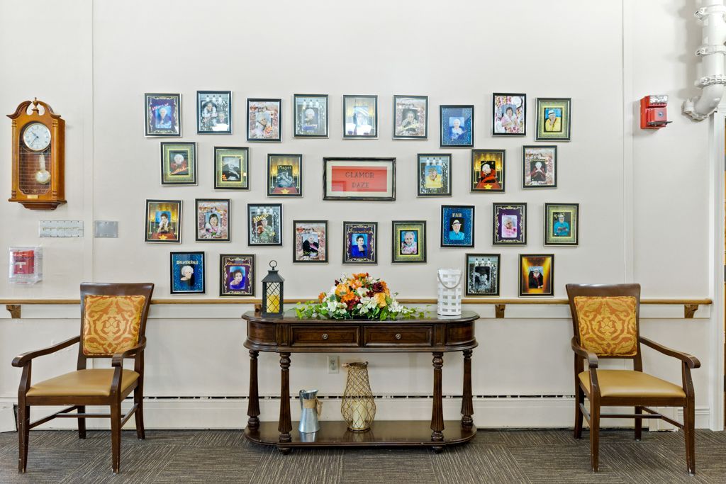 Wall with framed art, table with flowers, two chairs, and a clock.