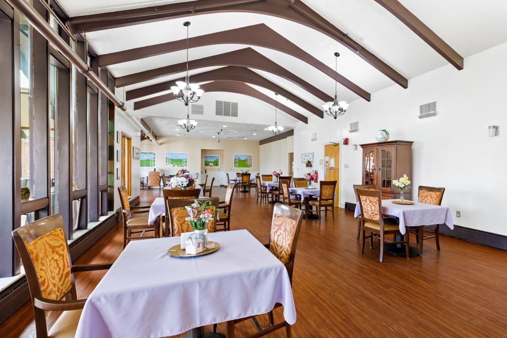 Dining room with tables, chairs, and artwork on the walls; wooden floor and ceiling beams.