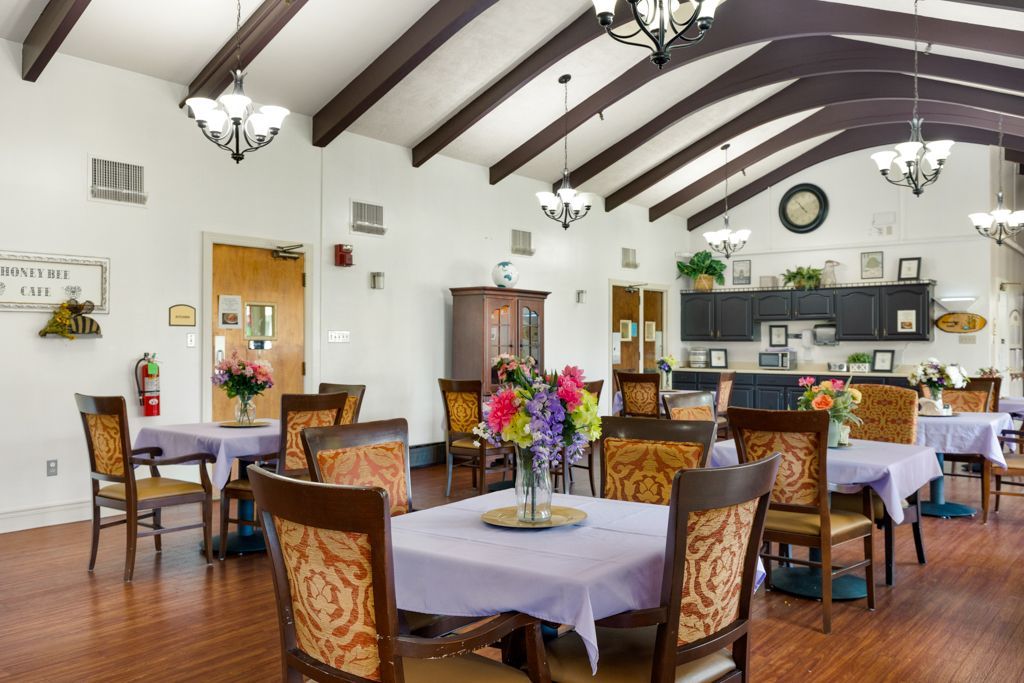 Dining room with tables set for meals, floral centerpieces, wood flooring, and exposed beams.