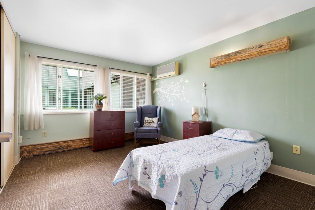 Bedroom with bed, chair, and dresser. Green walls, window with blinds.