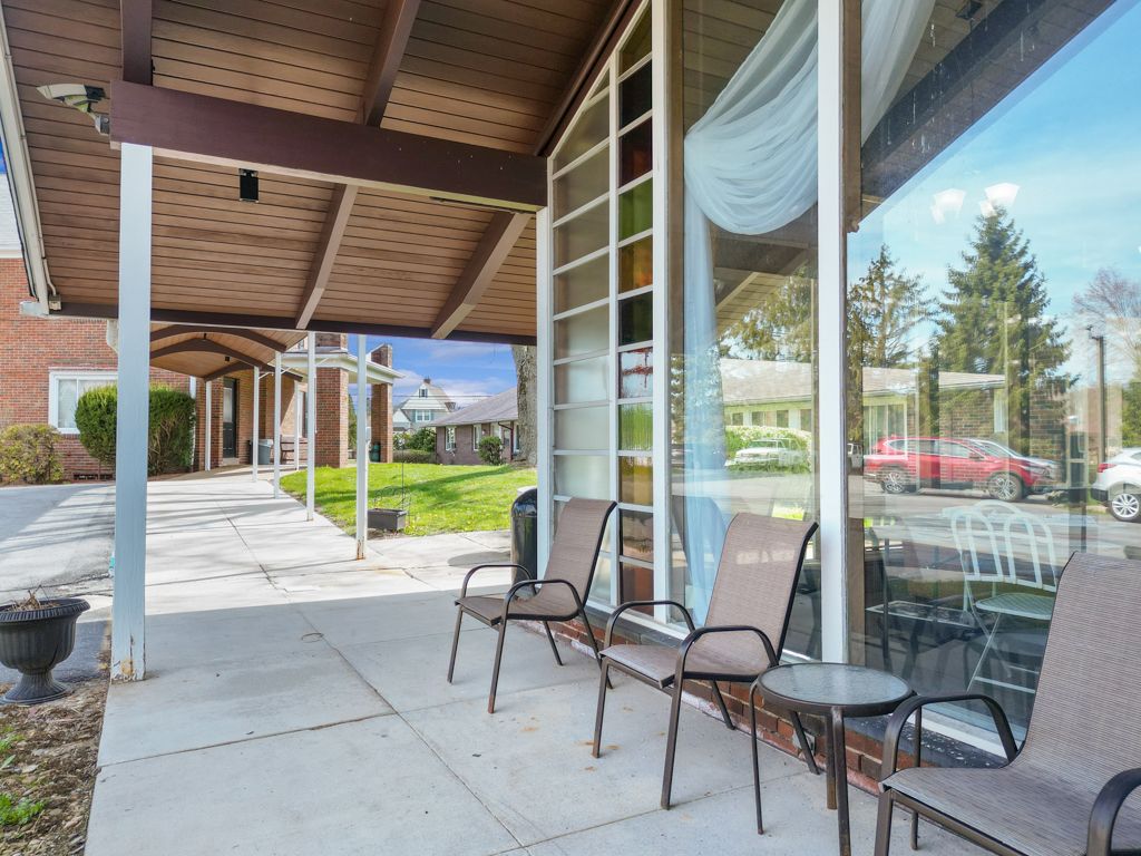 Covered outdoor seating area with chairs, a small table, and a large window.