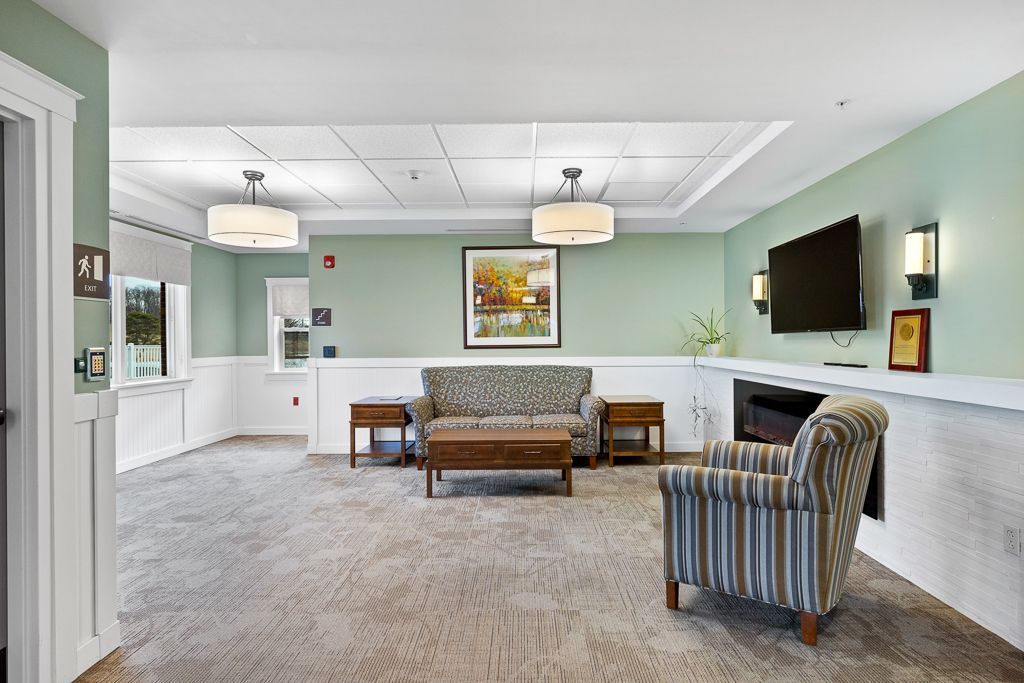Lounge with seating, fireplace, and television. Soft green walls, neutral carpet, and two hanging lights.