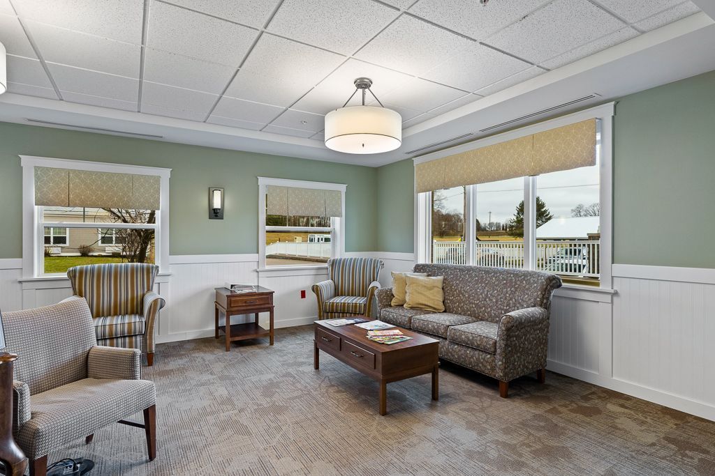 Waiting room with patterned armchairs and sofa, coffee table, windows, and a hanging light fixture.