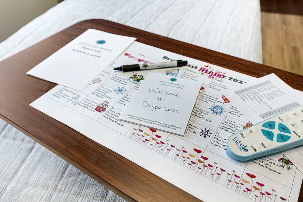 A wooden tray on a bed with papers, a pen, and a remote. Papers have notes and drawings in various colors.