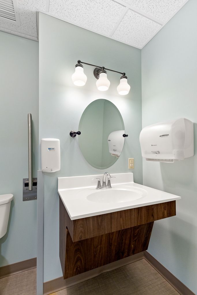 Accessible bathroom with a sink, mirror, and hand dryer. Teal walls and grab bar.
