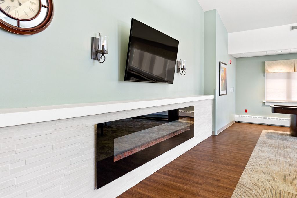 Wall with mounted TV, fireplace, clock, sconces, and artwork; light blue wall with brown flooring.