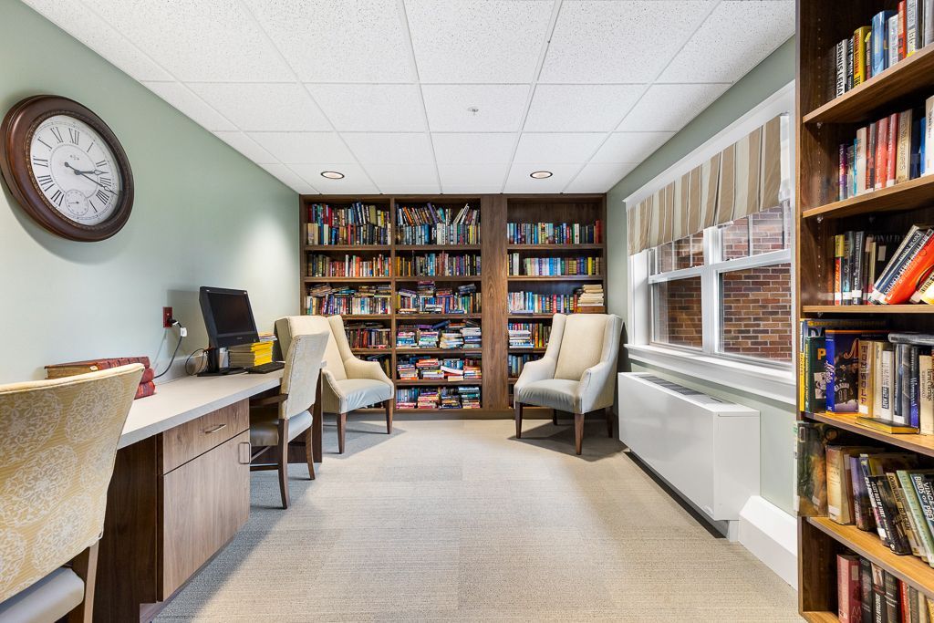 Library with bookshelves, seating, desks, and a clock. Soft colors and warm lighting.