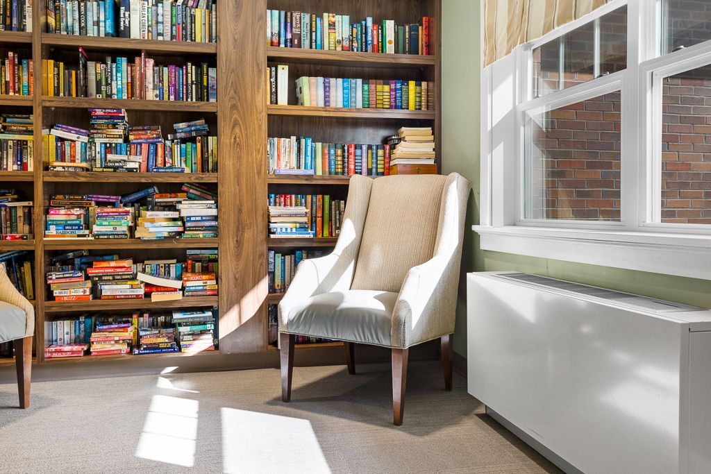 Cozy library reading nook with a chair, window, and bookshelves full of books.
