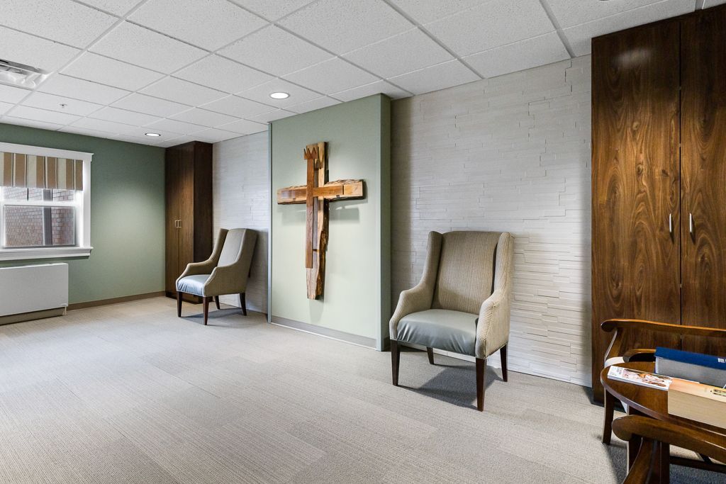 A room with a wooden cross, two armchairs, and a built-in cabinet.
