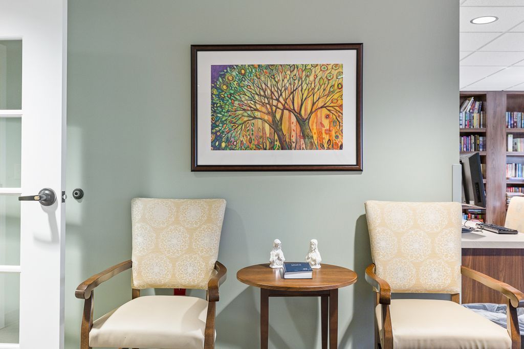 Two armchairs face each other, with a small table and art on a green wall. A library is visible in the background.