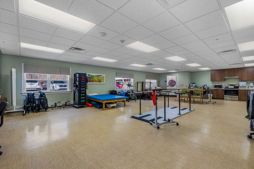 Physical therapy room with exercise equipment: parallel bars, treadmill, weights.
