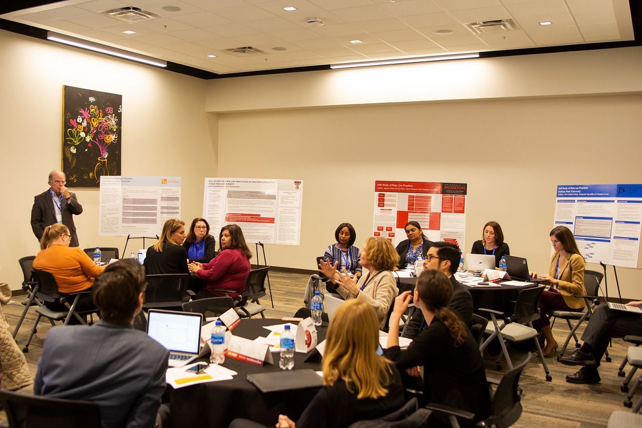 Educators seated at round tables during a US PREP working session, with research posters displayed on the wall behind them
