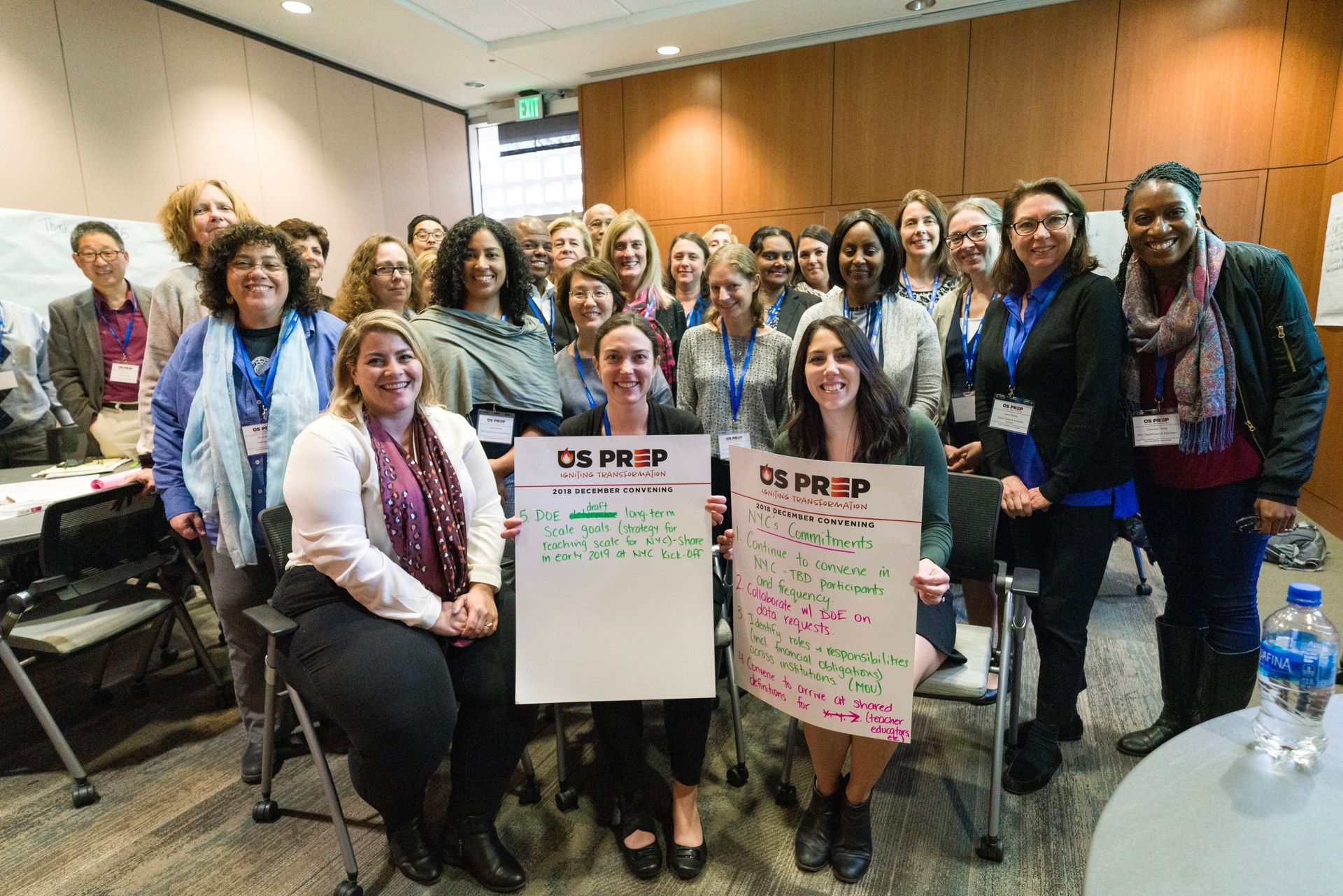 A large group of US PREP partners and educators gathered together, two of them holding handwritten US PREP posters