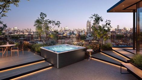 Rooftop terrace with glowing hot tub, lounge seating, and city skyline at dusk