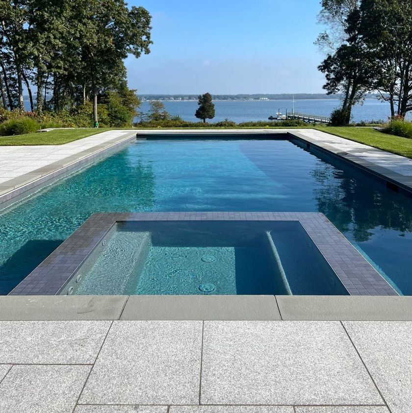 Modern infinity pool with a shallow sun shelf overlooking a calm lake and trees