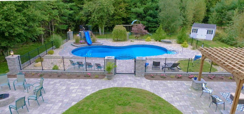 Outdoor pool area with blue water, lounge chairs, patio tables, and surrounding greenery.