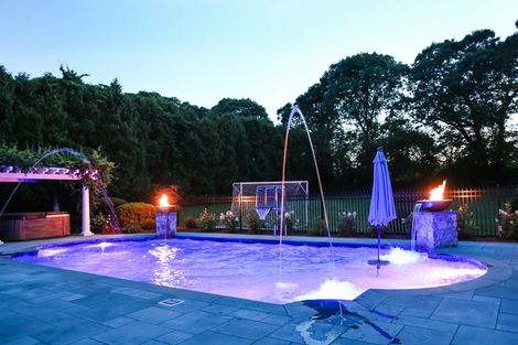 Lit backyard pool at dusk with fountains, torches, and a closed umbrella
