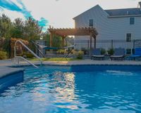 Backyard swimming pool with patio chairs, fence, and a white house at sunset