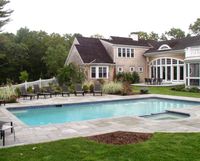 Backyard patio with a large blue swimming pool beside a house and garden seating area