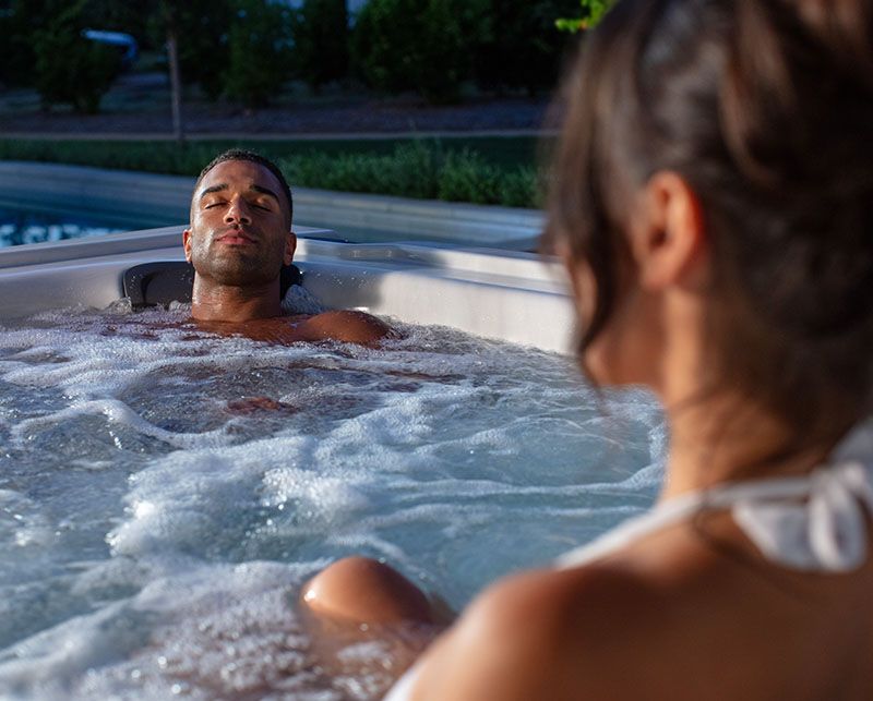 Two people relax in a bubbling outdoor hot tub at night