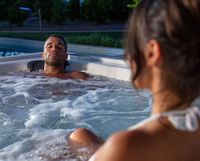 Two people relax in a bubbling outdoor hot tub at night