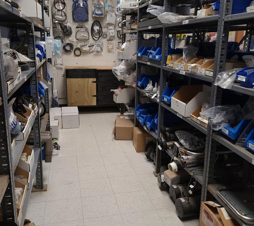 Narrow storage room aisle with metal shelves, boxes, tools, and parts on both sides