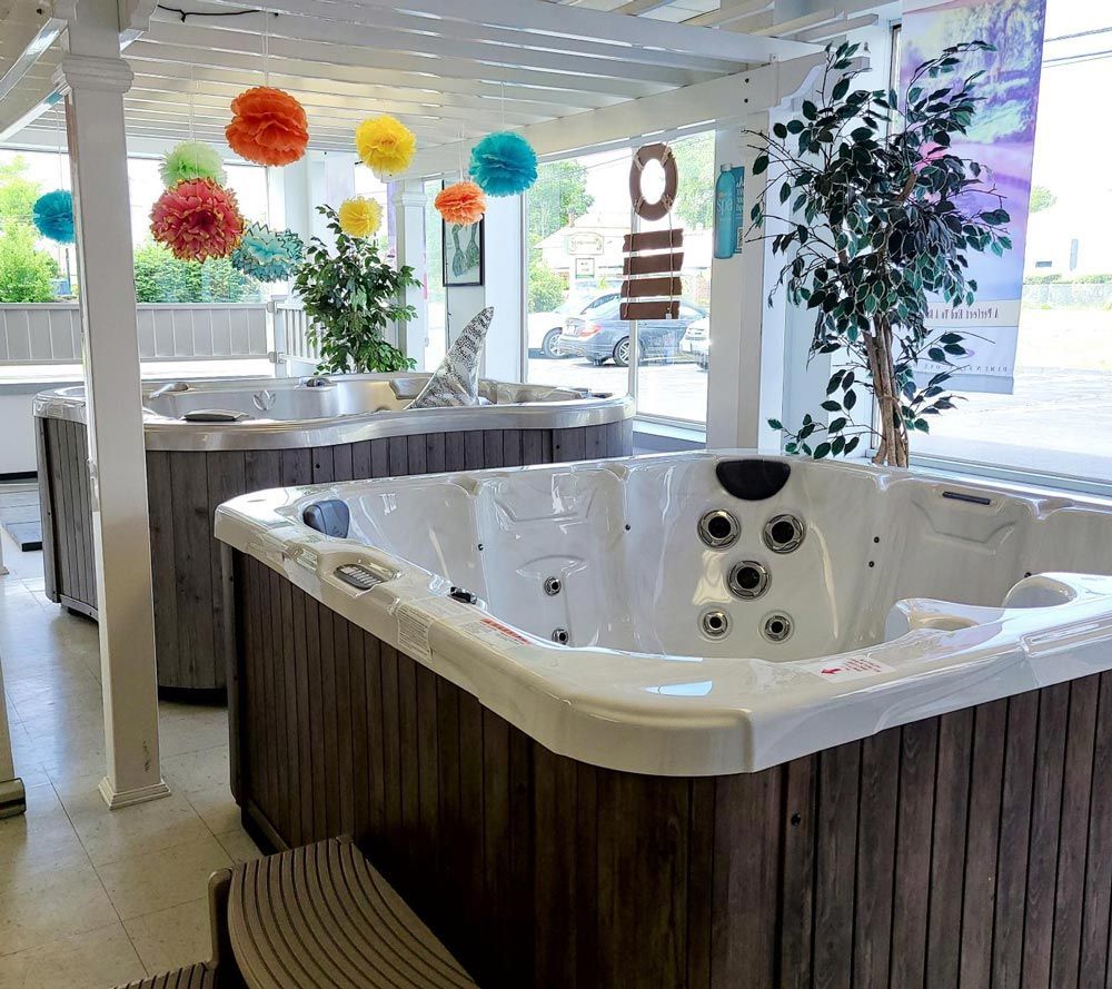 Bright spa showroom with a white hot tub, colorful hanging lights, and plants in a modern space