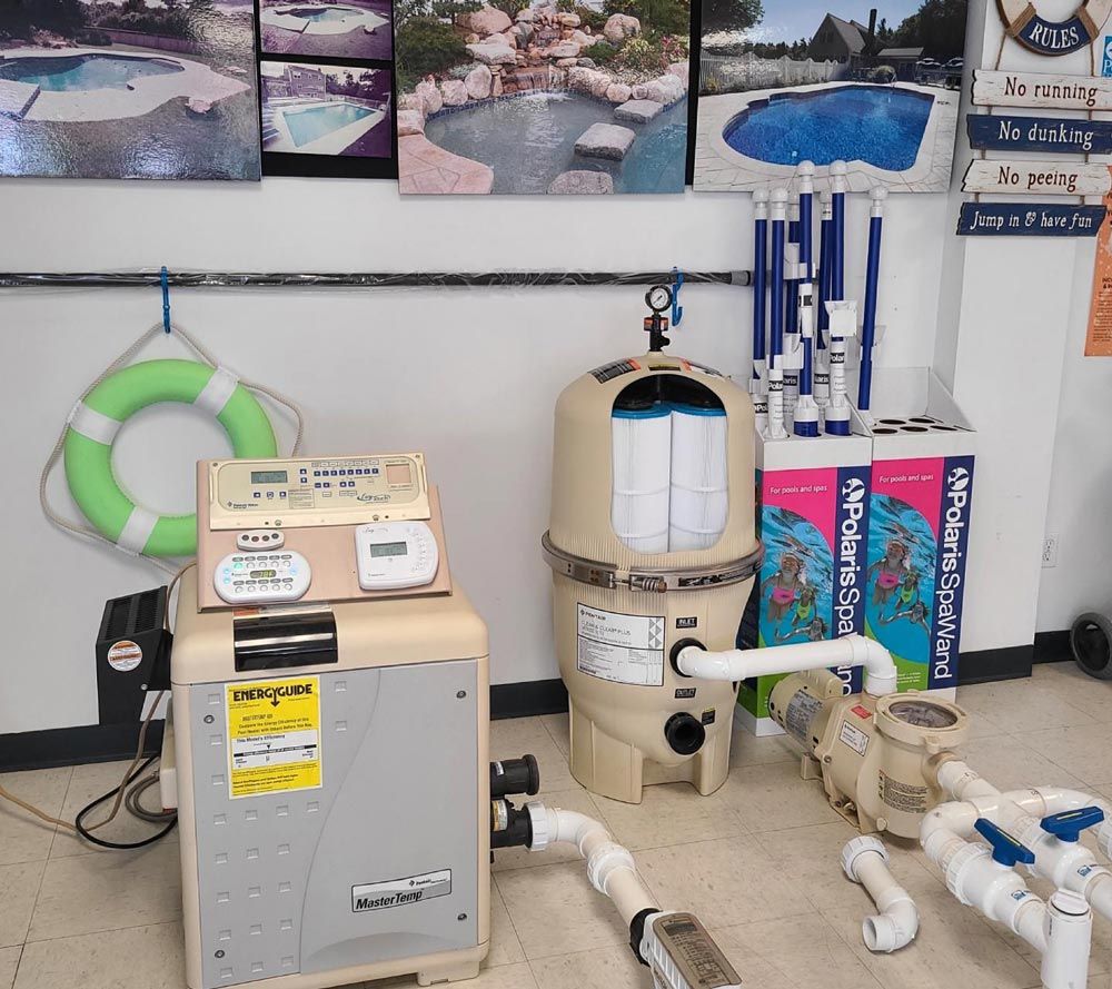 Pool equipment room with filters, pumps, pipes, and chemical tanks against a wall with pool photos.