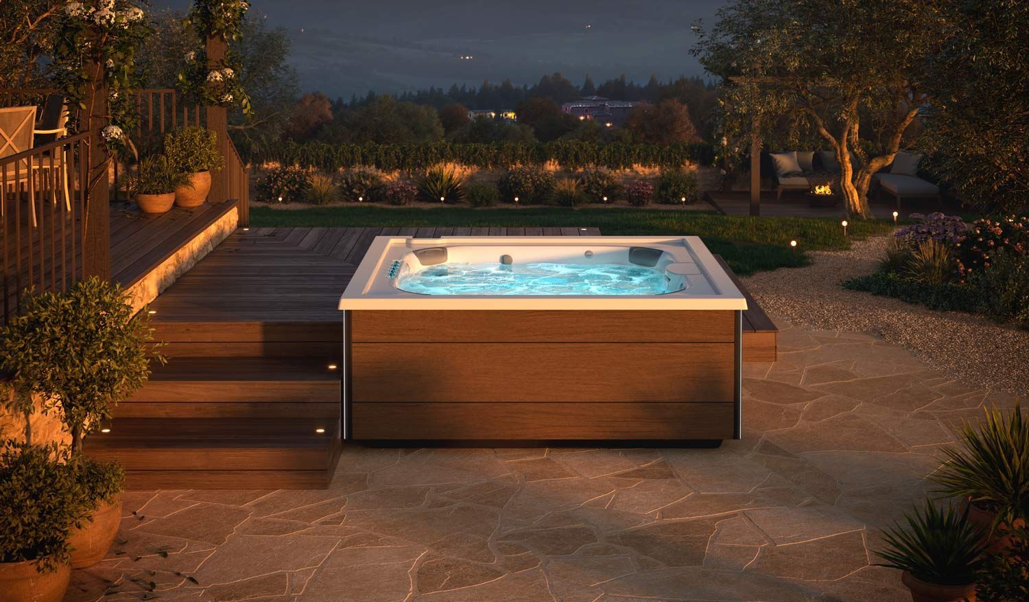 Backyard patio with a lit hot tub at dusk, surrounded by stone paving and garden landscaping