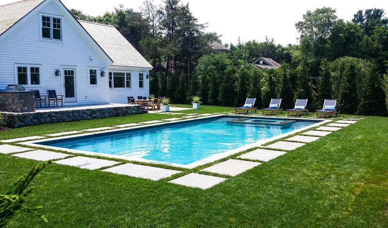 Backyard pool beside a white house with green lawn and lounge chairs