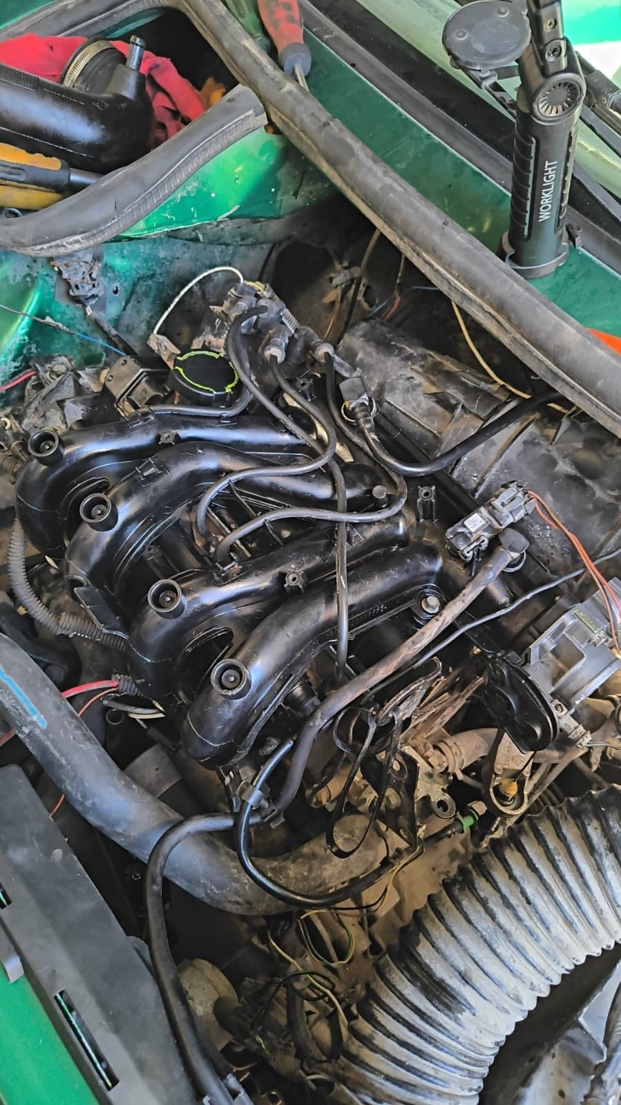 Compartimento del motor del coche con colector de admisión y mangueras negras expuestas, mostrando un motor parcialmente desmontado.