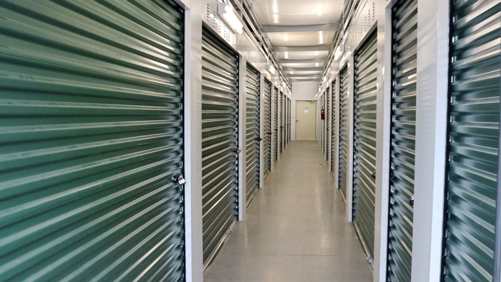 Interior of a storage unit facility. A long corridor with rows of green and white storage unit doors.