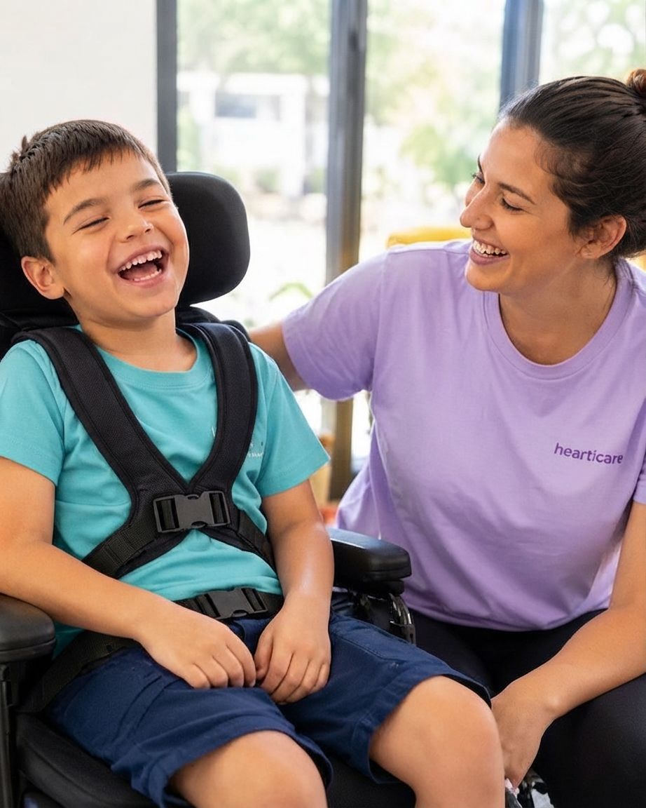 Smiling child in a wheelchair with a caregiver in a purple shirt beside them.