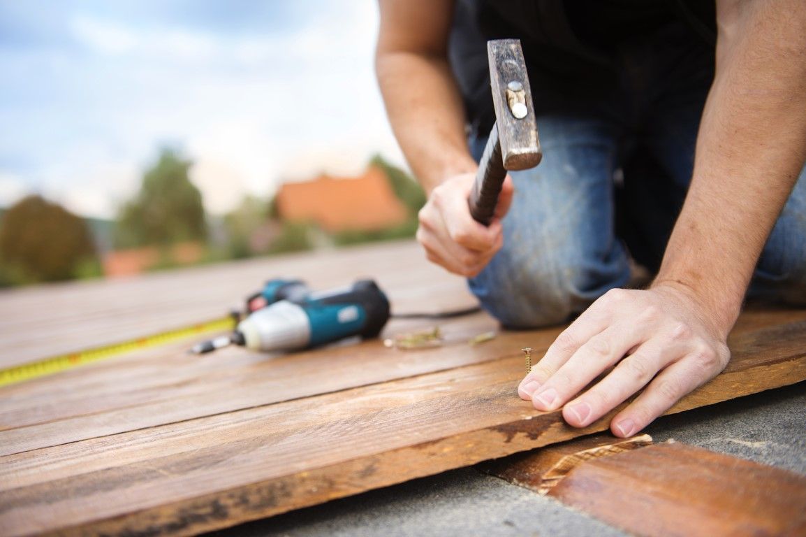 Person hammering a wooden deck plank outdoors with tools nearby
