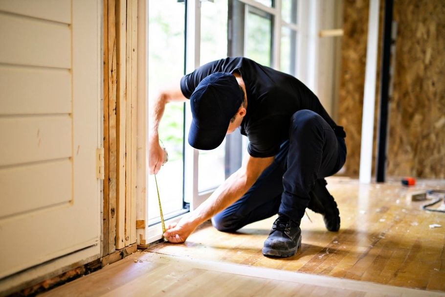 Person crouching by a doorway, inspecting or installing flooring in a sunlit room.